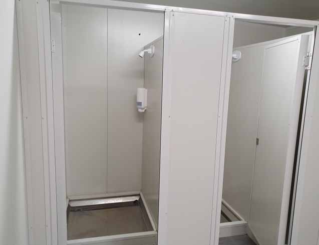 Interior of a multi‑shower ablution block with two cubicles, vinyl flooring and stainless‑steel fixtures.