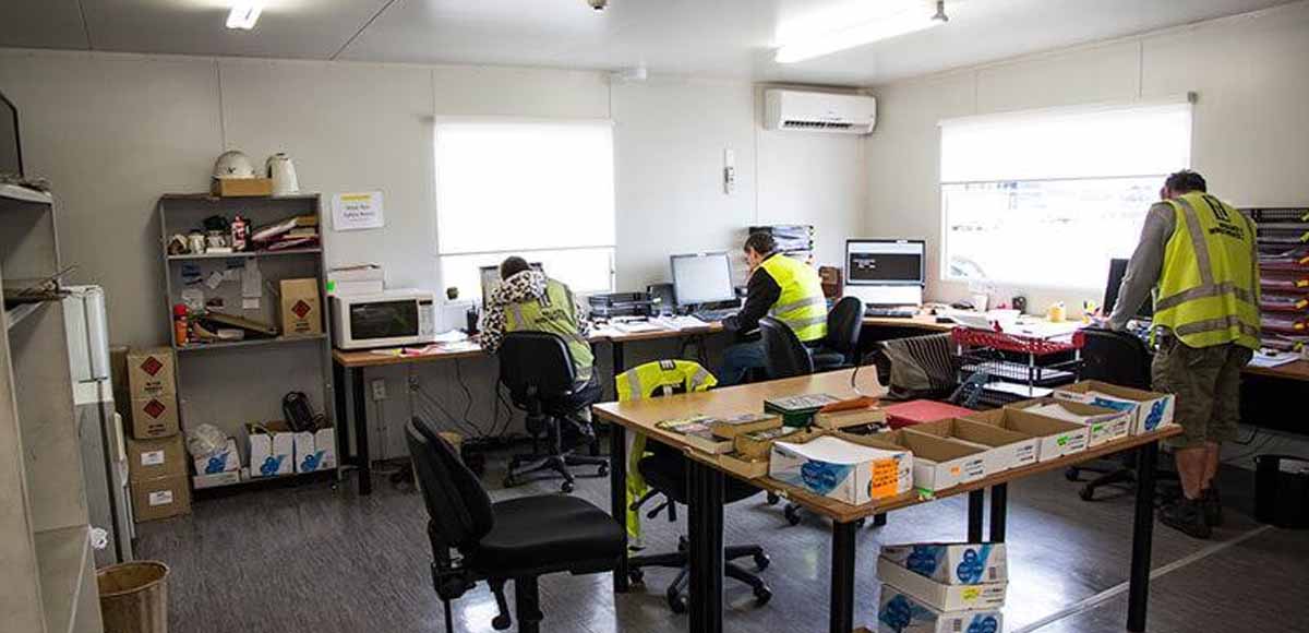 Crew working inside a portable site office with a wall-mounted air conditioning unit